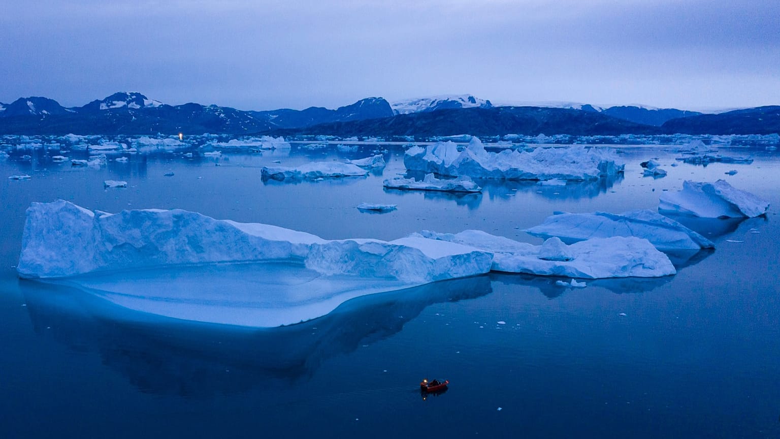Nesta fotografia de 15 de agosto de 2019, um barco navega à noite junto a grandes icebergues perto da cidade de Kulusuk, no leste da Gronelândia. 