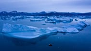 In this Aug. 15, 2019, photo, a boat navigates at night next to large icebergs near the town of Kulusuk, in eastern Greenland. 