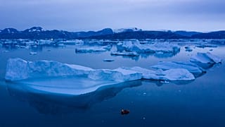 15 Ağustos 2019 tarihli bu fotoğrafta, Grönland'ın doğusundaki Kulusuk kasabası yakınlarında büyük buzdağlarının yanında geceleyin seyreden bir tekne görülüyor. 