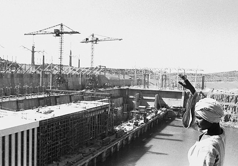 Un ouvrier égyptien salue en se tenant au sommet d'un rocher surplombant la centrale électrique partiellement construite sur le haut barrage d'Assouan, le 27 février 1968. 