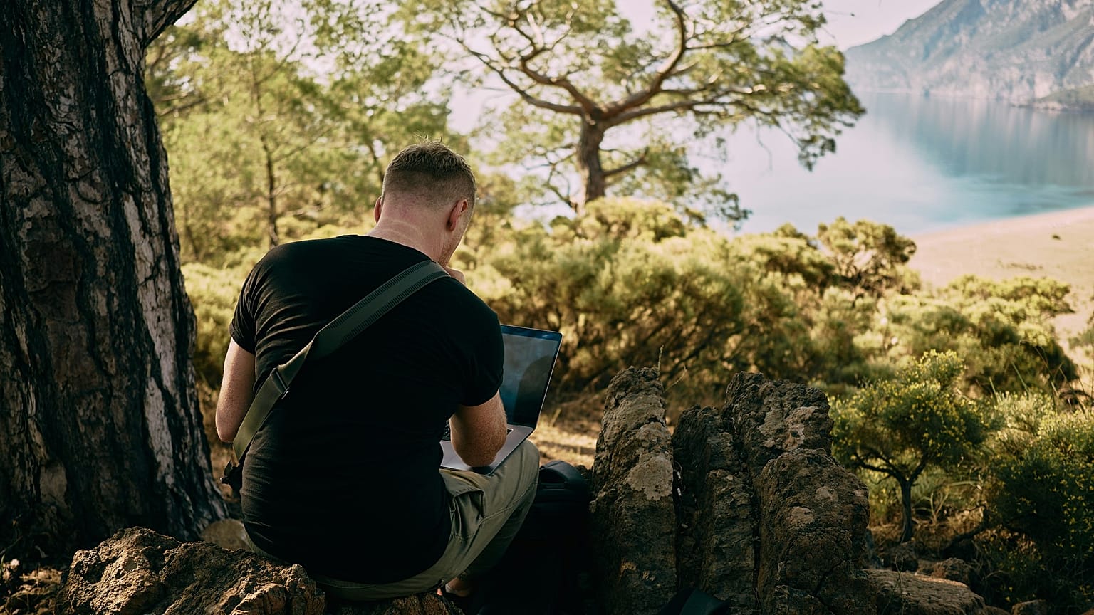 A man working on his laptop in front of a beach.