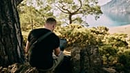 A man working on his laptop in front of a beach.