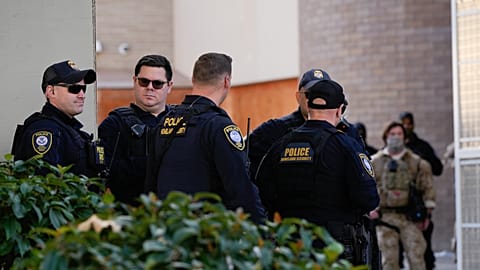 Law enforcement officers wait by the gates of a United States Immigration and Customs Enforcement (ICE) facility as other officers talk with protesters in Portland, Ore., Mond