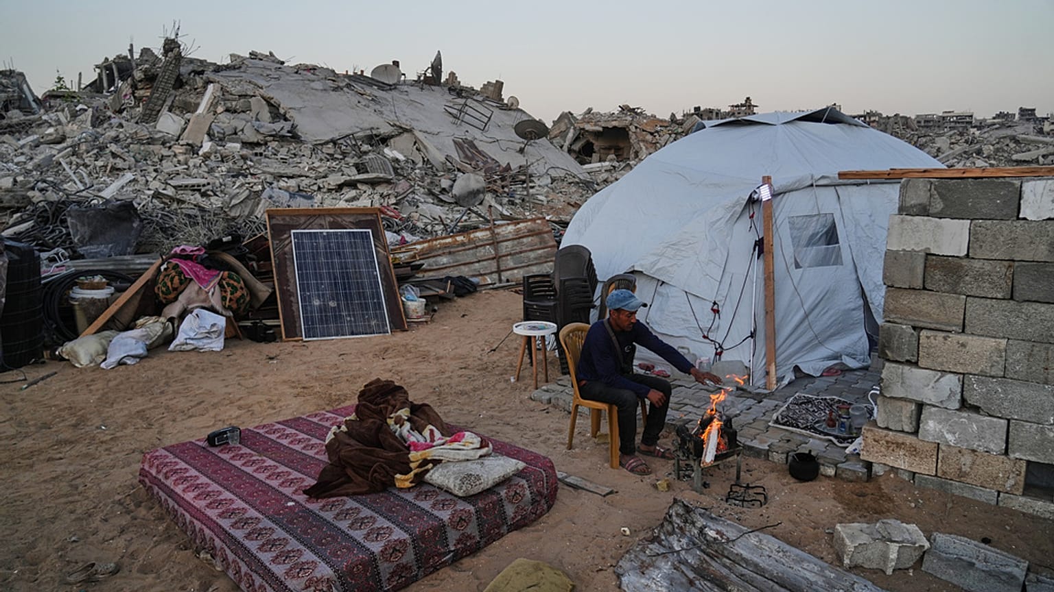 O palestiniano deslocado Belal Al-Yaziji senta-se junto a uma fogueira no exterior da sua tenda, no meio da destruição provocada pela ofensiva aérea e terrestre israelita no bairro de Sheikh Radwan.