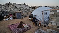 Displaced Palestinian Belal Al-Yaziji sits by a fire outside his tent amid the destruction left by the Israeli air and ground offensive in Sheikh Radwan neighborhood.