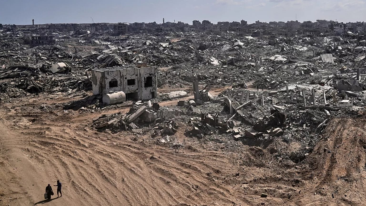 Due sfollati palestinesi camminano davanti a edifici distrutti nel quartiere di Sheikh Radwan, pesantemente danneggiato, a Gaza City, 11 ottobre 2025.