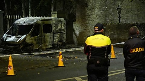 Сотрудники полиции стоят на месте сгоревшего полицейского автомобиля рядом с отелем Citywest в Дублине, 22 октября 2025 года.