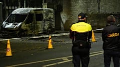 Des policiers de la Garda Síochána se tiennent sur les lieux de l'incendie d'une voiture de police.