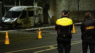 Garda Siochana police officers stand at the scene of a burned out police vehicle.