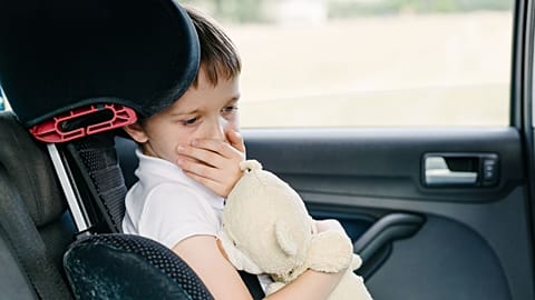 A child coughs into his hand in the car.