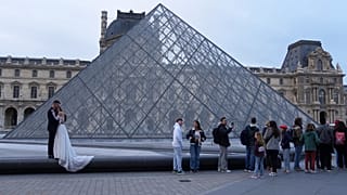 يحتضن زوجان بعضهما البعض بينما يصطف الزوار لدخول متحف اللوفر، الأربعاء 22 أكتوبر/تشرين الأول 2025 في باريس.