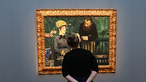 A woman views the painting "In the Conservatory" by Edouard Manet