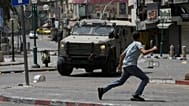 یک فلسطینی در جریان درگیری با نیروهای اسرائیلی پس از یک حمله نظامی در شهر نابلس در کرانه باختری، روز ۲۷ اوت ۲۰۲۵، در مقابل یک خودروی زره‌پوش می‌دود.