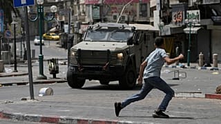 یک فلسطینی در جریان درگیری با نیروهای اسرائیلی پس از یک حمله نظامی در شهر نابلس در کرانه باختری، روز ۲۷ اوت ۲۰۲۵، در مقابل یک خودروی زره‌پوش می‌دود.