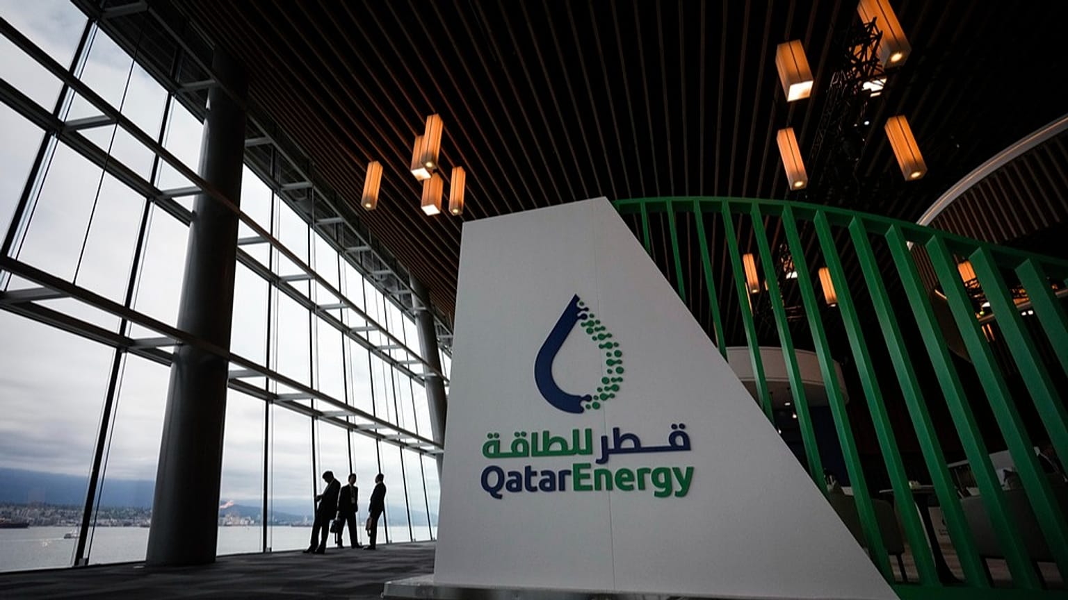 Delegates are silhouetted as they take in the view of the harbour while talking near the Qatar Energy booth during the opening ceremony at the LNG2023 conference