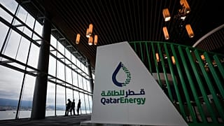 Delegates are silhouetted as they take in the view of the harbour while talking near the Qatar Energy booth during the opening ceremony at the LNG2023 conference