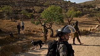 Israeli settlers stand near members of Israeli forces blocking access for Palestinians to an area for harvesting olives in the West Bank village of Sa'ir, 23 October, 2025