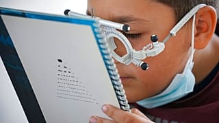 صبي يقرأ نصًا باستخدام نظارات فحص البصر أثناء فحص البصر الذي أجراه أطباء عيون متطوعون يعملون مع منظمة "كاسا بونا" الإنسانية، أو "البيت الصالح"، في نوكسوارا، رومانيا