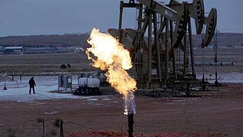 عمال يعملون على مضخات النفط خلف لهب غاز طبيعي