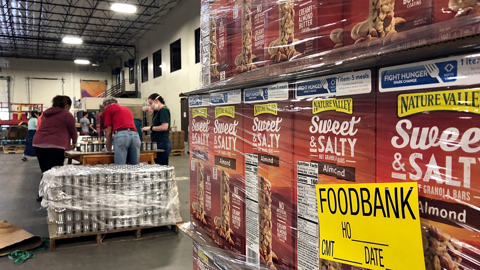 FILE - A pallet of food awaits processing as volunteers work in the background to label cans of beans for redistribution at Food Bank in Albuquerque, N.M., May 7, 2020.
