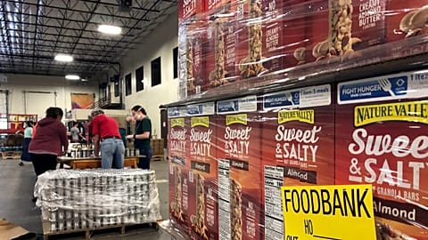 FILE - A pallet of food awaits processing as volunteers work in the background to label cans of beans for redistribution at Food Bank in Albuquerque, N.M., May 7, 2020.