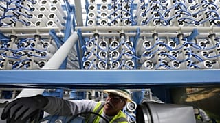 عامل يقوم بضبط معدات بين نحو ألفي وعاء ضغط سيتم استخدامها لتحويل مياه البحر إلى مياه عذبة عبر تقنية التناضح العكسي (تصوير: غريغوري بول / أسوشيتد برس)