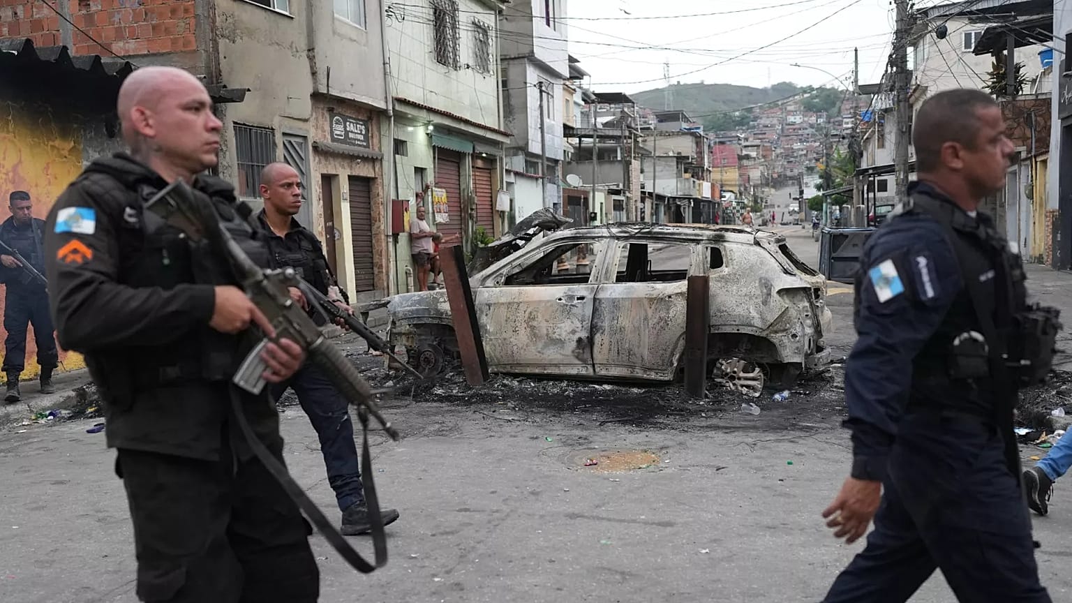 Police walk past a burned car used as a roadblock during a police operation against alleged drug traffickers in the Complexo do Alemao favela.