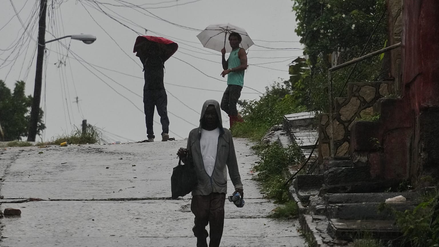 People walk under the rain before the arrival of Hurricane Melissa in Santiago de Cuba, Tuesday, Oct. 28, 2025. (AP Photo/Ramón Espinosa)