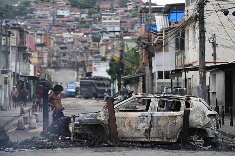 Des personnes retirent les pièces utiles d'une voiture incendiée utilisée comme barricade par des trafiquants de drogue présumés lors d'une opération policière dans la favela.