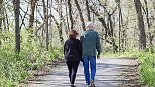 An older couple walk through the woods.