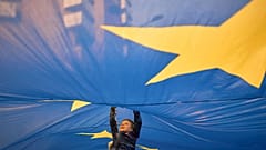 ARQUIVO - Uma criança salta para debaixo de uma bandeira da União Europeia durante uma manifestação pró-UE antes da segunda volta das eleições presidenciais em Bucareste, na Roménia. maio de 2025