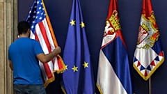 Um membro do pessoal do protocolo arruma as bandeiras dos EUA, da UE e da Sérvia em Belgrado, na Sérvia.