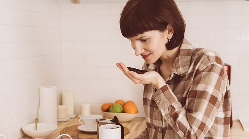 امرأة تستنشق رائحة حبوب القهوة في مطبخها.