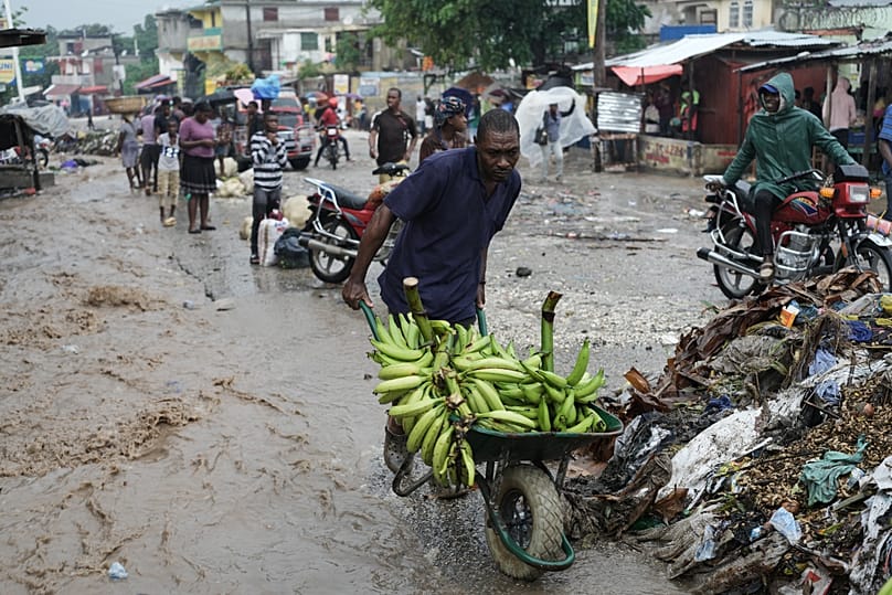 A an pushes a wheelbarrow through a flooded street in the aftermath of Hurricane Melissa in Petit-Goave, Haiti, Thursday, Oct. 30, 2025.