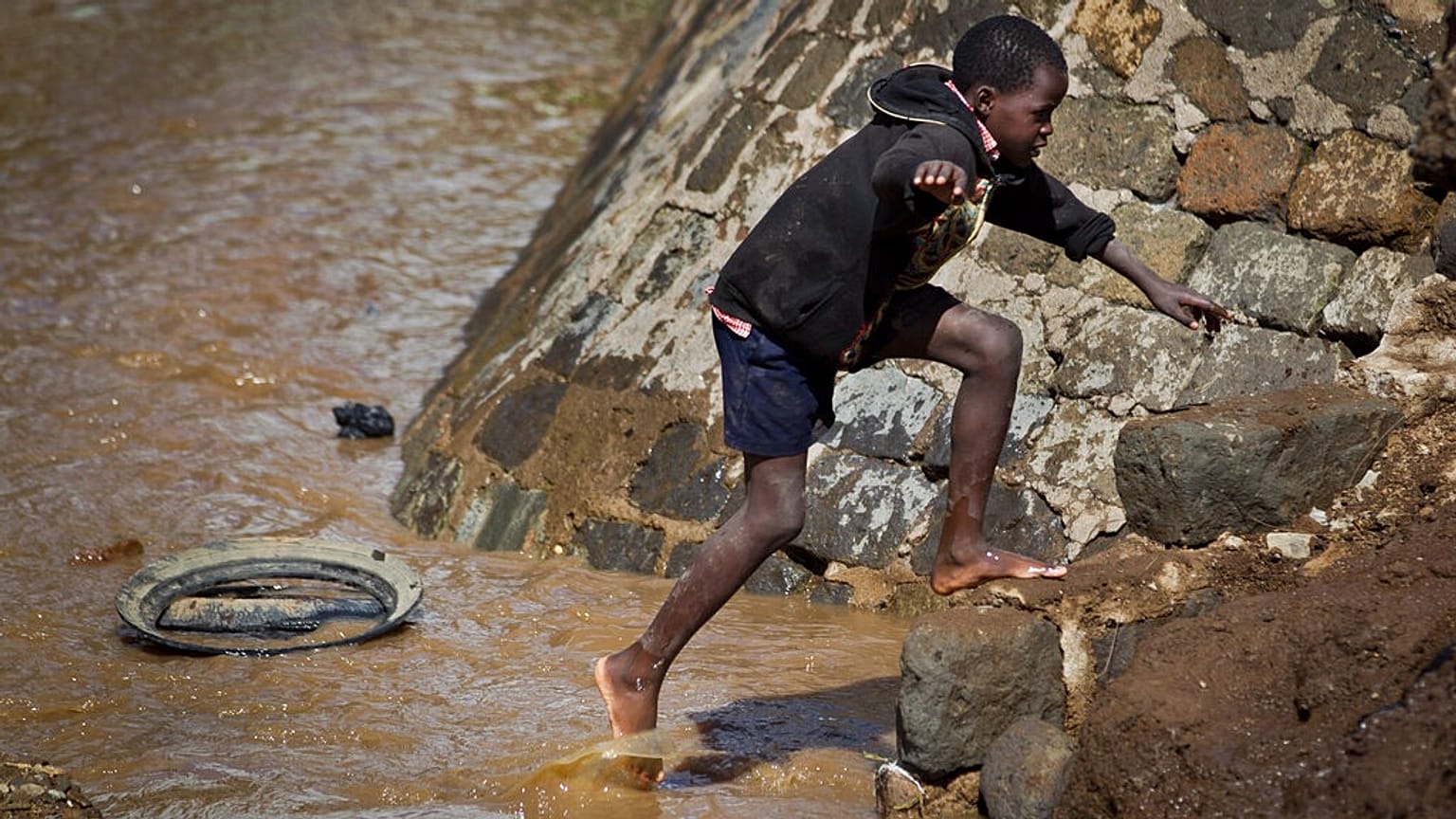 FILE - A barefoot boy crosses a flooded drainage channel following heavy rains in recent days, in a market-area of the town of Narok, Kenya Thursday, April 18, 2013