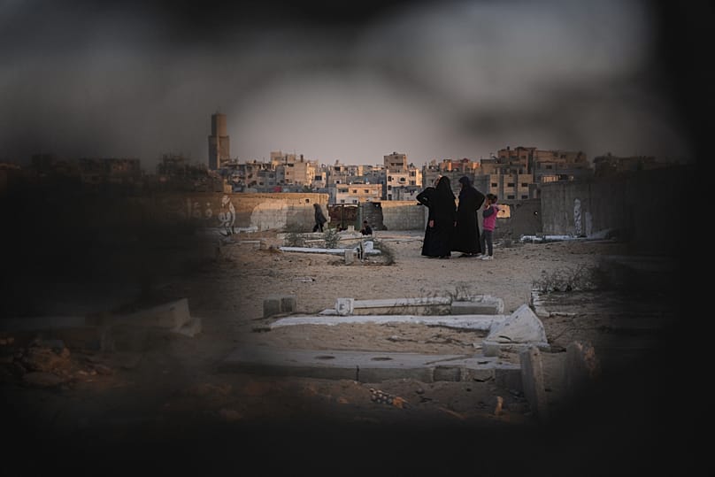Palestinian women stand at a cemetery in Khan Younis where a makeshift tent camp for displaced people was set up, 31 October, 2025