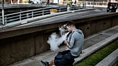 رجل يستخدم سيجارة إلكترونية ويزفر دخانها أثناء جلوسه في شارع بوسط مدينة لوس أنجلوس