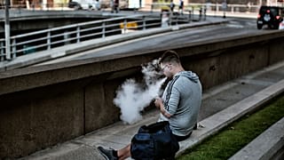 رجل يستخدم سيجارة إلكترونية ويزفر دخانها أثناء جلوسه في شارع بوسط مدينة لوس أنجلوس