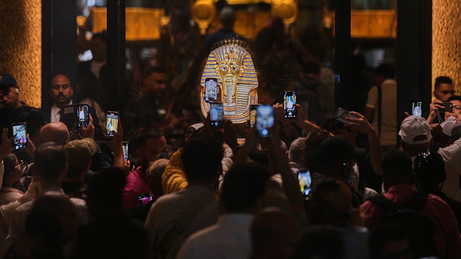  أشخاص يحملون أجهزة محمولة أمام قناع الدفن الذهبي للملك توت عنخ آمون خلال اليوم الأول للزوار بعد الافتتاح الرسمي للمتحف المصري الكبير في الجيزة، مصر، الثلاثاء 4 نوفمبر 2025. 