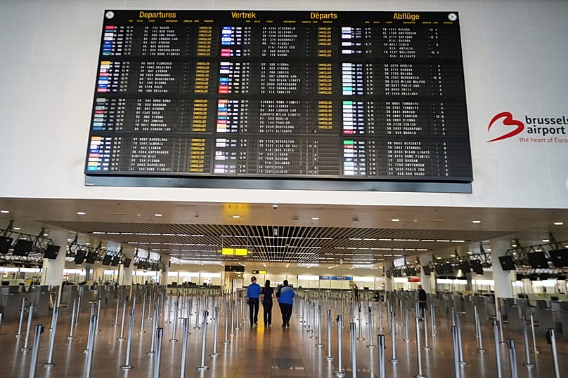Employees walk through an empty terminal with a departure board of cancelled flights at Brussels International Airport in Zaventem, 14 October, 2025