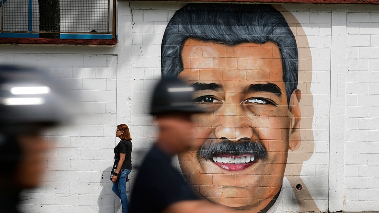 جدارية للرئيس الفنزويلي نيكولاس مادورو تغطي أحد جدران الشوارع بينما يمر سائقو دراجات نارية بجانبها في كراكاس، فنزويلا، الخميس 5 حزيران/يونيو 2025.