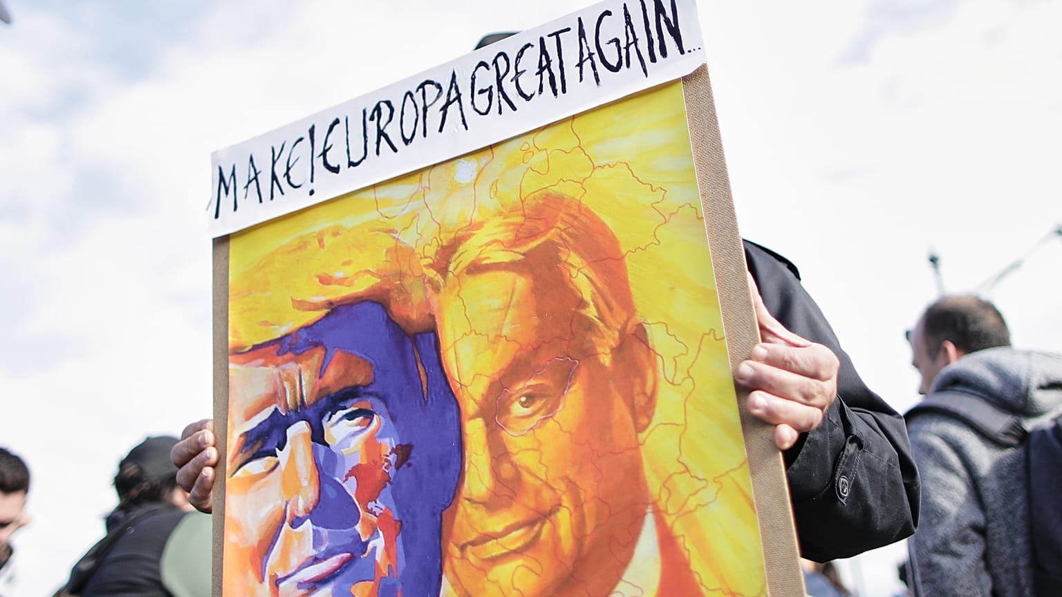 Egy kormánypárti tüntető Donald Trump amerikai elnök és Orbán Viktor magyar miniszterelnök rajzait ábrázoló táblát tart a 69. évforduló alkalmából rendezett ünnepségen.