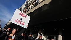 Un manifestante regge un manifesto con la scritta "Shame on Shein" (Vergogna su Shein) davanti ai grandi magazzini BHV, dove è stato aperto il primo negozio permanente della società di fast fashion Shein. Parigi. 5 novembre 2025.