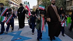 Ein Geistlicher, Schüler und andere Demonstrierende treten auf ein Bild der Israelflagge mit blutendem Davidstern bei einer jährlichen Kundgebung vor der früheren US-Botschaft