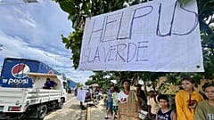 Einwohner von Isla Verde stehen neben einem Schild, das sie als Hilferuf auf dem Weg zu ihren beschädigten Häusern angebracht haben, nachdem der Taifun Kalmaegi in den Gemeinden Verwüstungen angerichtet hat.