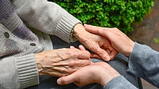 An older person holds hands with their caregiver.