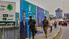 سكان محلّيون يمرّون قرب لافتة تدعو إلى مقاطعة الانتخابات في مدينة الصدر بضواحي بغداد، 22 أكتوبر 2025.