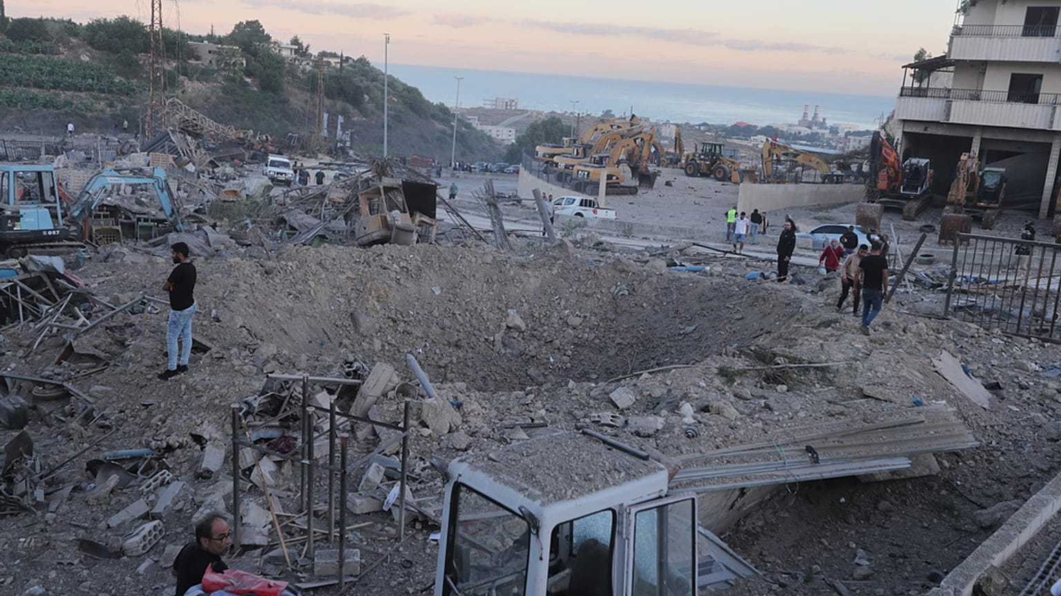 يتجمع الناس بالقرب من حفرة ناجمة عن غارات جوية إسرائيلية استهدفت موقعًا لبيع المعدات الثقيلة، في قرية المصيلح الجنوبية، لبنان، السبت 11 أكتوبر/تشرين الأول 2025.