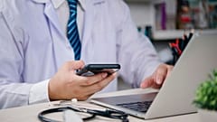 Eine medizinische Fachkraft prüft ihr Smartphone. Am Laptop arbeitet sie.