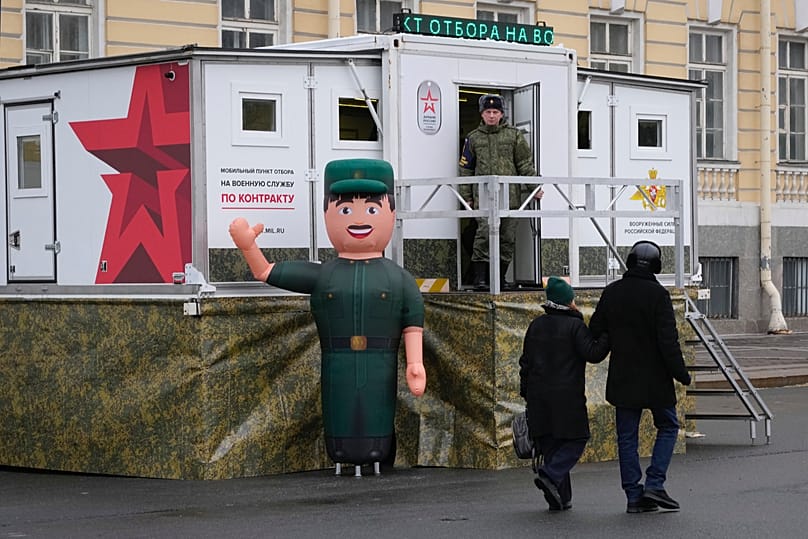 FILE: People walk past a mobile recruiting center set up near a military-historical exhibition in St. Petersburg, Russia, Saturday, Jan. 27, 2024